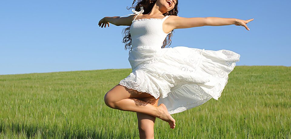 Happy woman twirling with white dress in a field